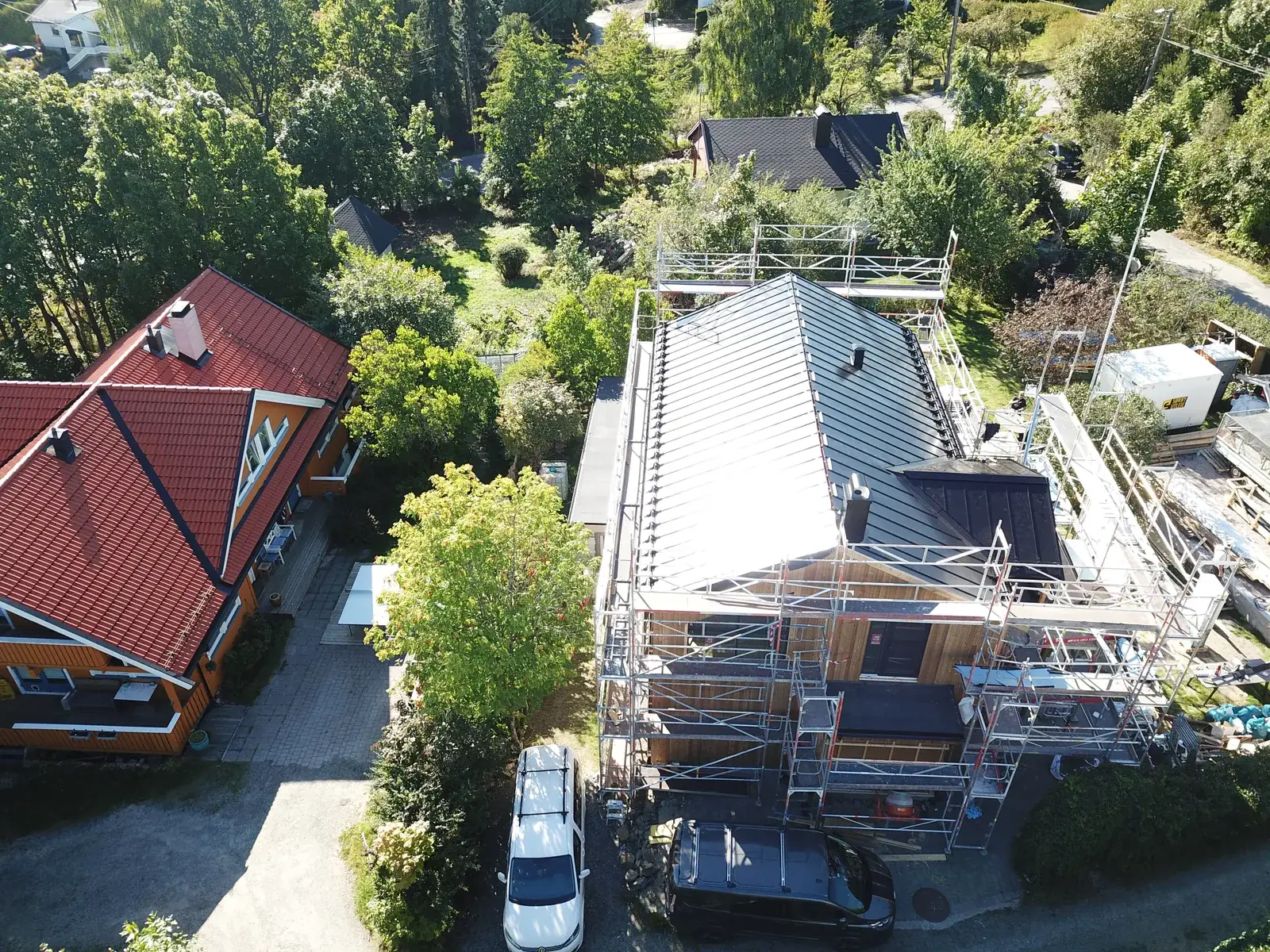 Luftfoto av enebolig med nytt lyst metalltak og stillas rundt bygget